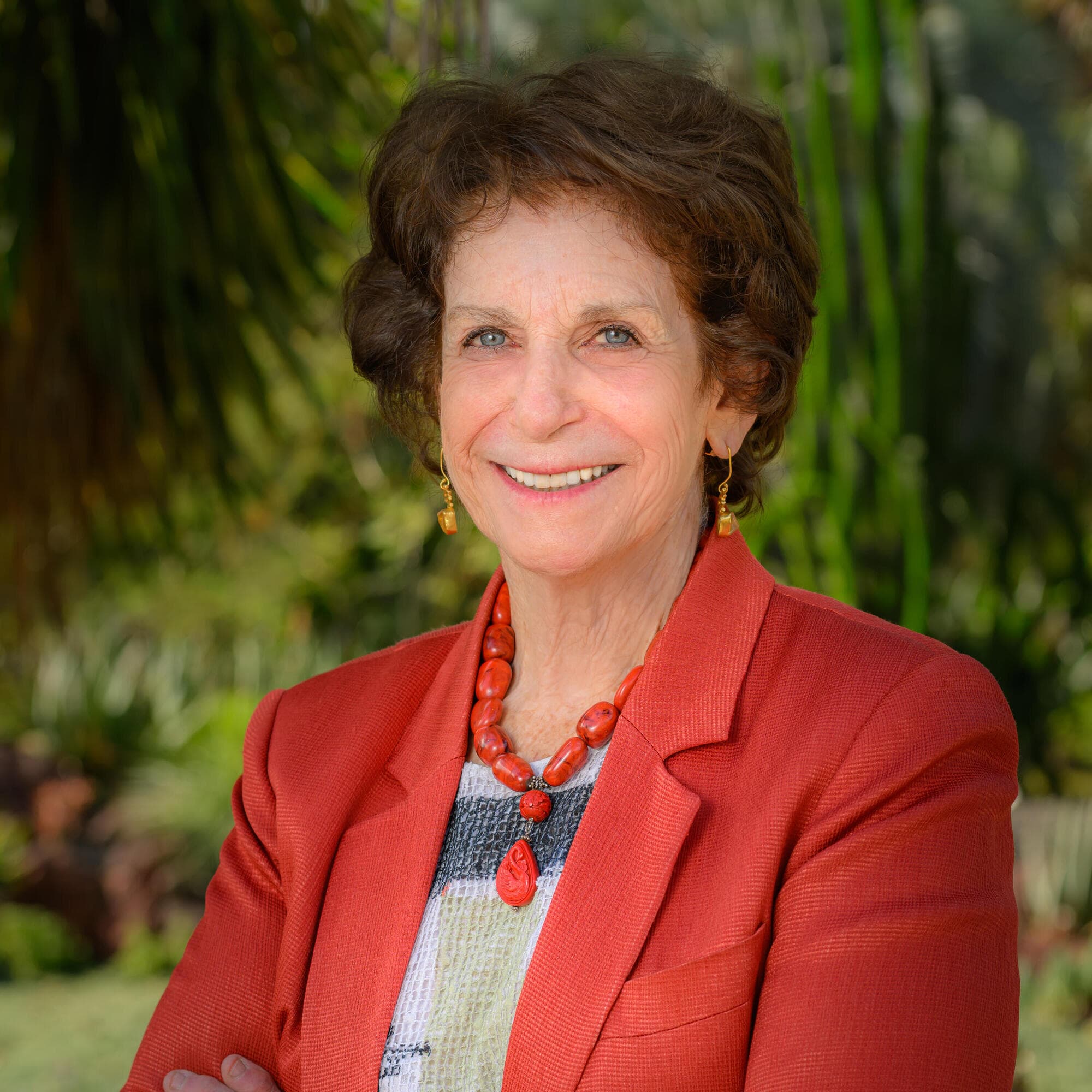 Huntington President Karen R. Lawrence poses for a portrait photo, standing outdoors with arms crossed wearing a terracotta-colored blazer.