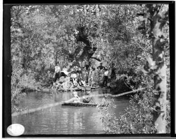 Boys and girls in a boat and on the shore at a pond