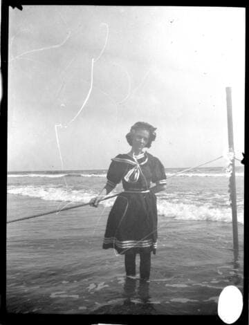 A young lady in a bathing dress wading in the water at the beach