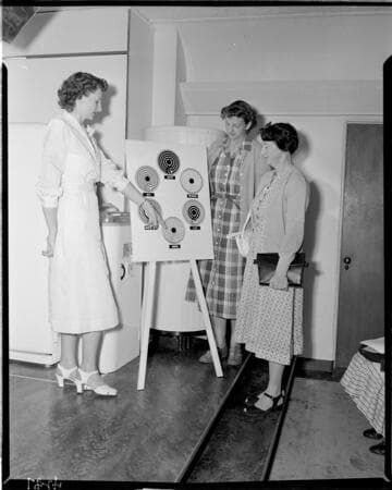 Woman demonstrating hot plate adjustments for an electric range to two lady customers