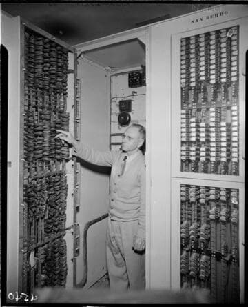 Man at back of heavily wired switchgear panel