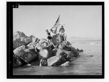 Two women posing with flag on breakwater at the Yacht Harbor Breakwater dedication, Santa Monica