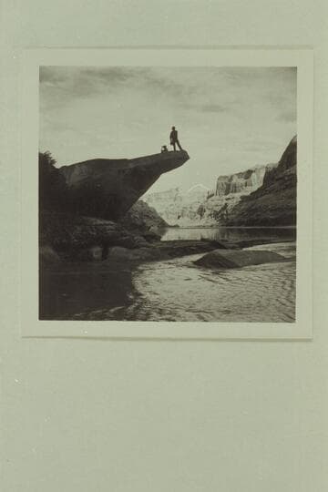 Preston Mercer standing on rock on river side of the mouth of the Escalante River.  Sally Van Valkenburg sits on the rock