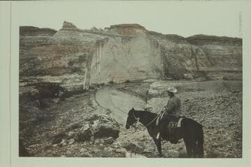 A. C. Ekker looks back from the Angels Trail to the cliff opposite the mouth of Robbers Roost Canyon