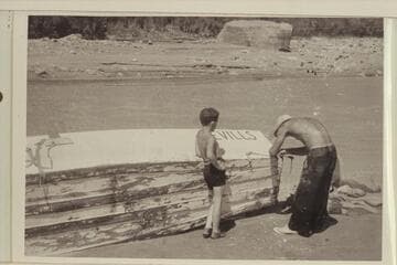 Norm Nevills repairing boat (?) after hitting rock, probably Nokai (?) Rapids.  Jackie Frost watches