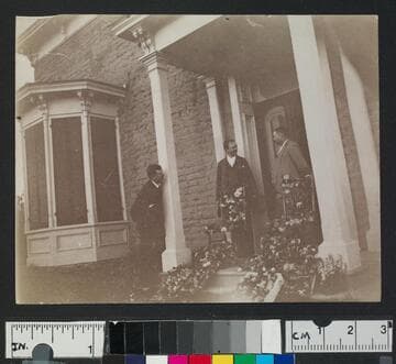 Three men in front of a building with flowers strewn over chairs