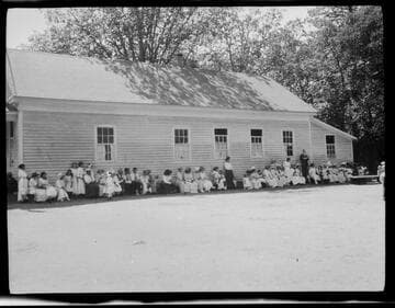 Adults and children in front of a school [?] building