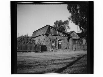 Small adobe building with advertising signs posted on wall and door