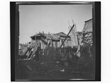 Adobe building held up by boards, with washing basin in yard
