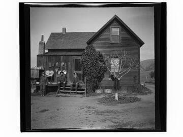 Three men in front of small wooden house with a coat hanging on a tree