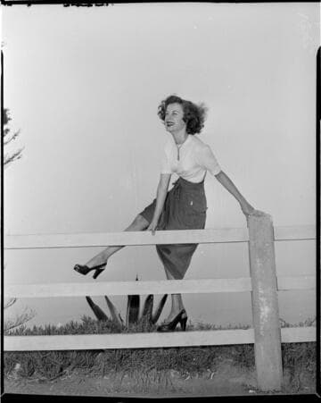 Young lady in a skirt on a fence rail overlooking the beach