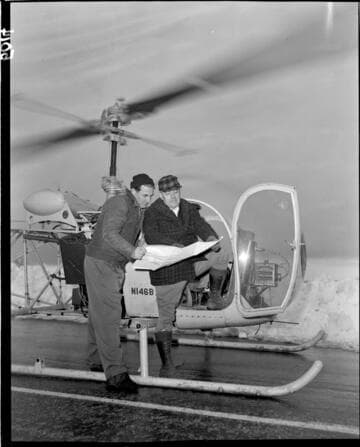 Pilot and passenger reviewing snow survey map at door of helicopter