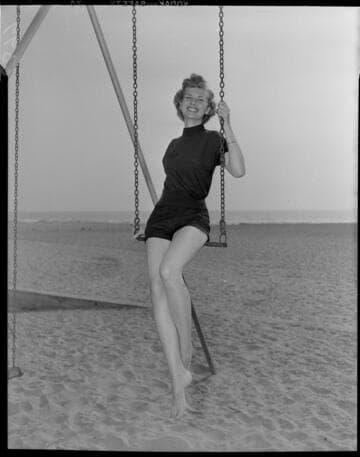 Young lady in shorts and polo shirt sitting on trapeese at the beach