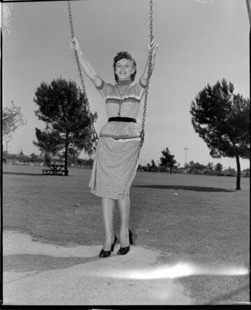 Young lady in a skirt and sweater posed sitting in a playground swing at a park