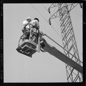 Two men going up in bucket to wash tower insulators