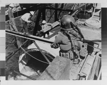 During construction of the Huntington Beach Steam Station in 1957, a deep sea diver prepares to descend to the ocean floor to guide a section of cooling water conduit into place