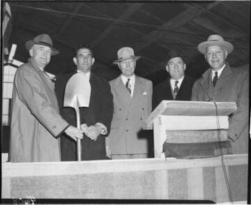 Five men at speakers stand with shovel for ground breaking