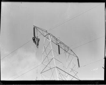 Men hanging from tower crossarm stringing conductor
