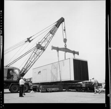 Crane lifting and transferring a large trailer crate between a railroad flatcar and a flatbed truck