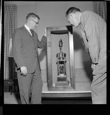 Two men standing by a large trophy