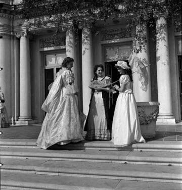 Three people in period costume on the terrace steps by the south entrance of the Huntington residence