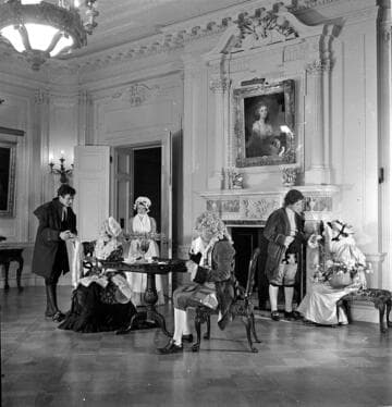 Six people in period costume in the dining room in the Huntington residence